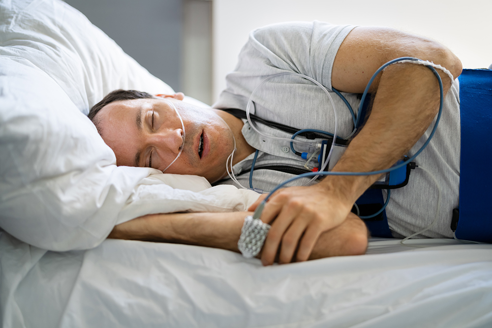 A man lying in bed being treated by At-home Sleep Studies with monitoring equipment