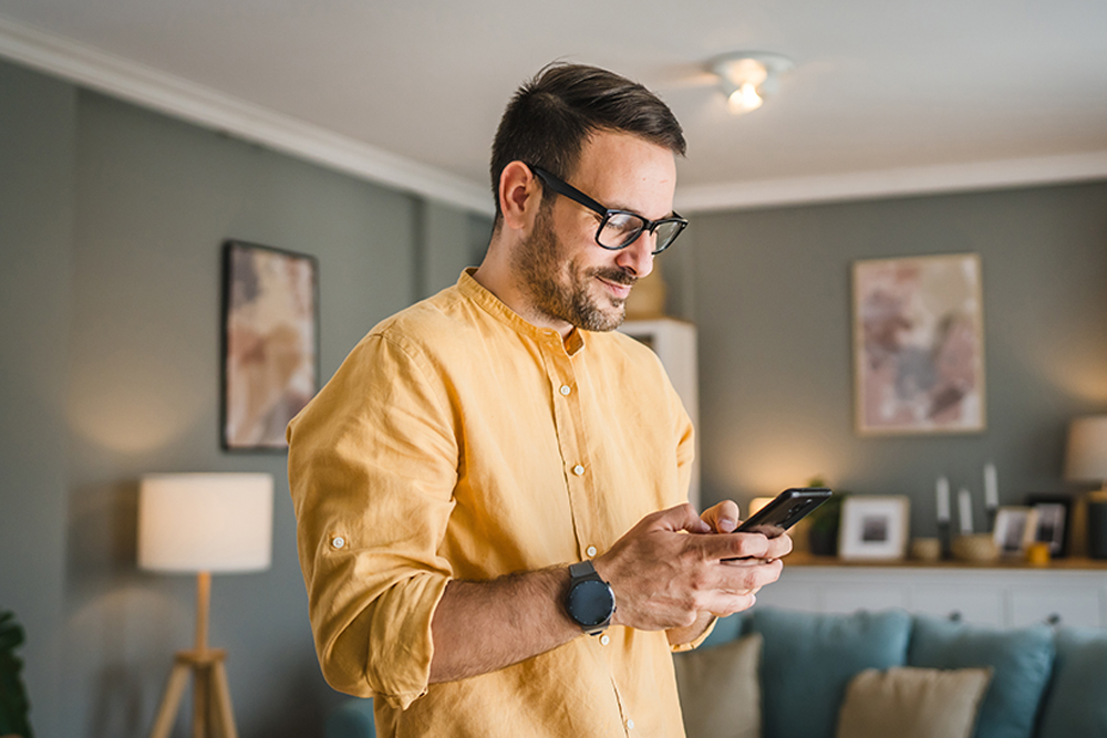 A man wearing glasses and a yellow shirt using a smartphone 