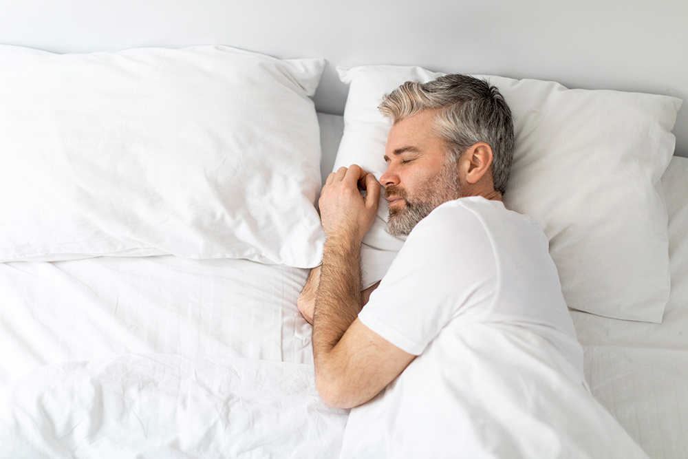 A man sleeping peacefully on a white bed